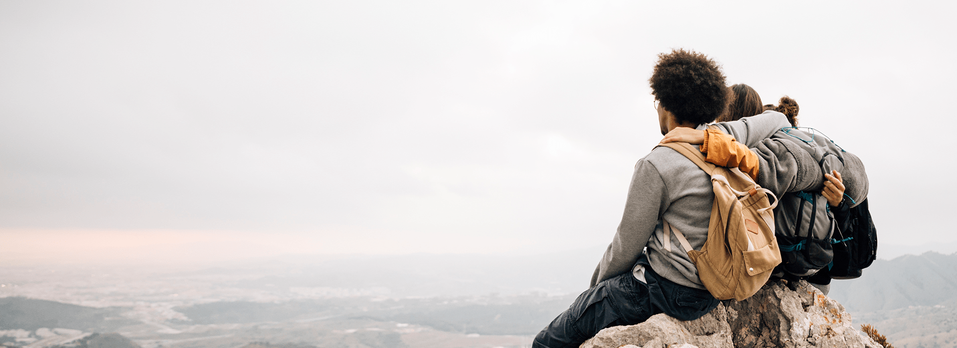 Hikers sitting on a mountaintop overlooking a vast plain