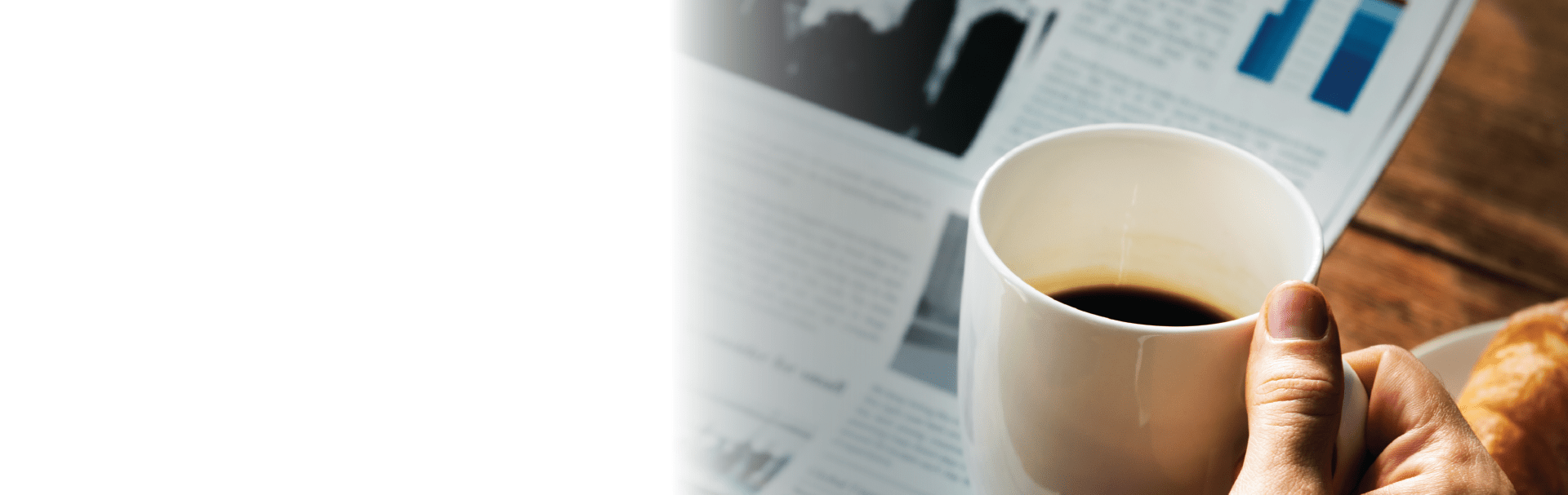 man reading newspaper with coffee cup and croissant